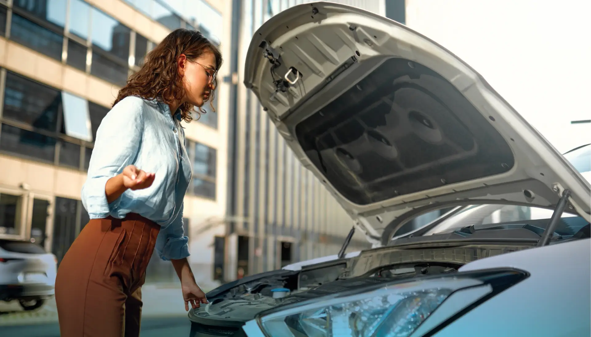 Women looking under her car's hood wondering how the engine parts function