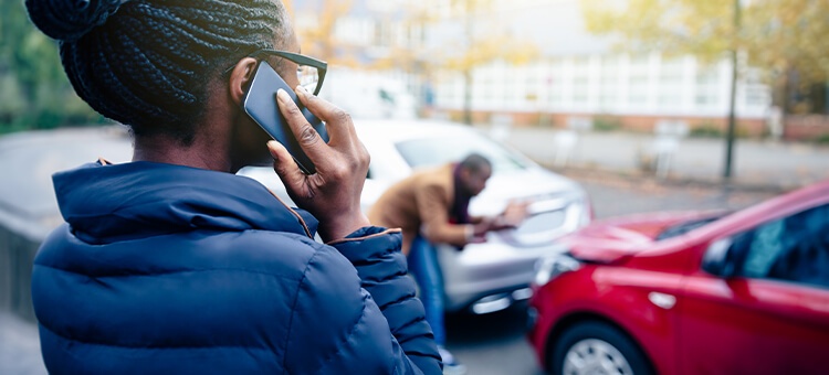 One person is on the phone, the second person is inspecting the damage after a collision, wondering if the car is written off