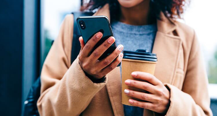A person with a phone and coffee in hand, learning about different car insurance terms
